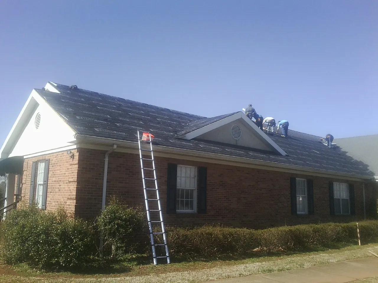 Crew tearing shingles off a brick ranch roof with a ladder set — Metal Roof Repair work by our crew in Surgoinsville