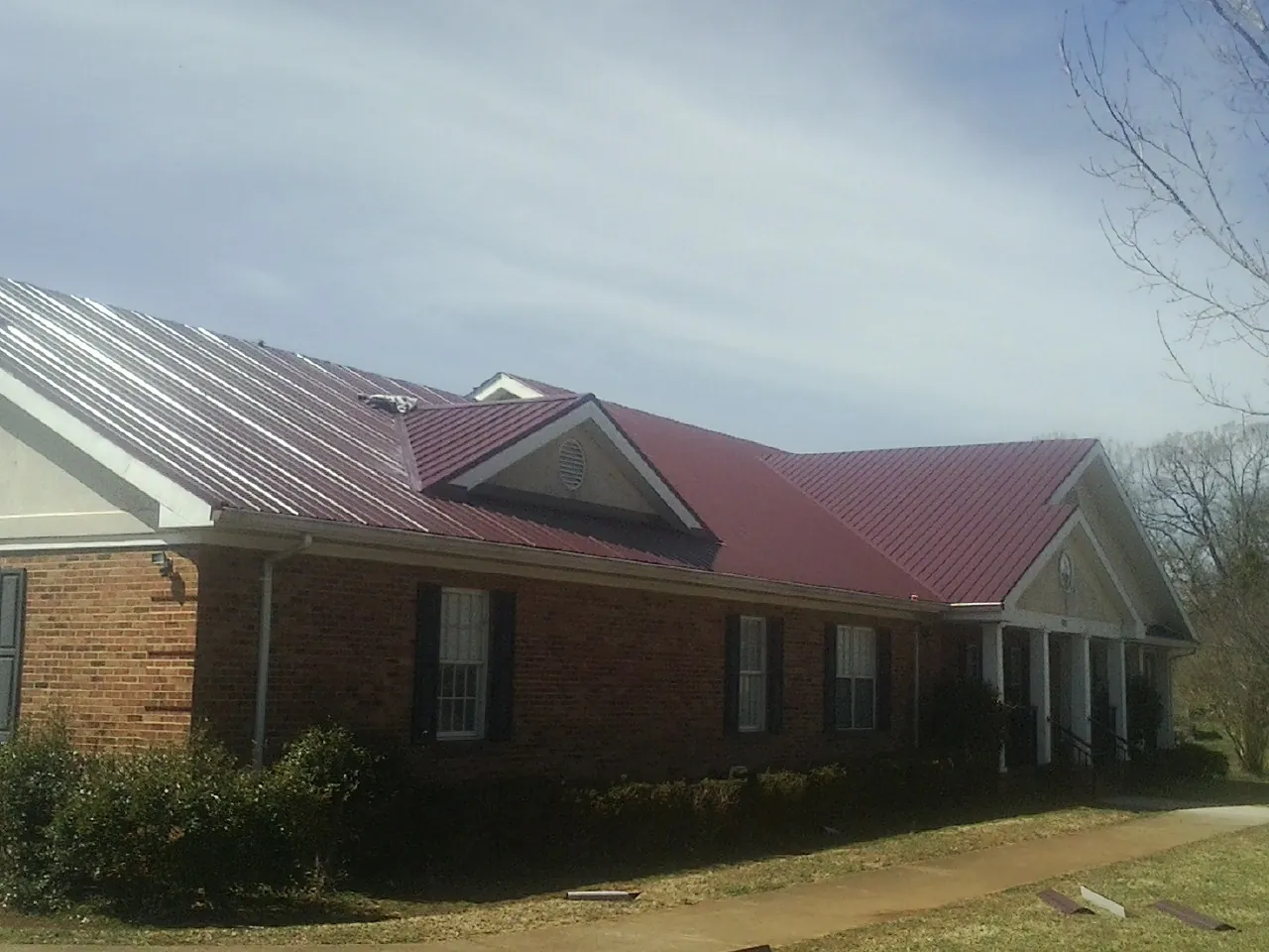 Red metal roof with gabled entries on a long brick building, from a Hail Damage Roof Repair job in Surgoinsville