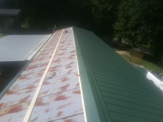 Old rusted panels beside newly installed green metal roofing — Wind Damage Roof Repair by Roofing Brothers in Surgoinsville