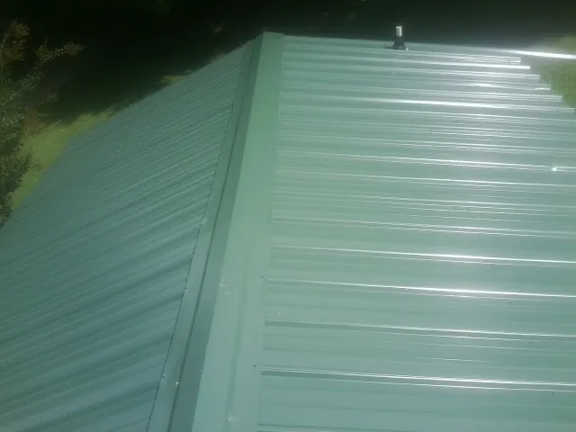 New green metal panels meeting at the ridge of a roof — Flat Roof Repair work by our crew in Surgoinsville