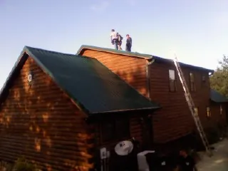Crew on the ridge of a green metal roof on a two story log home in Surgoinsville