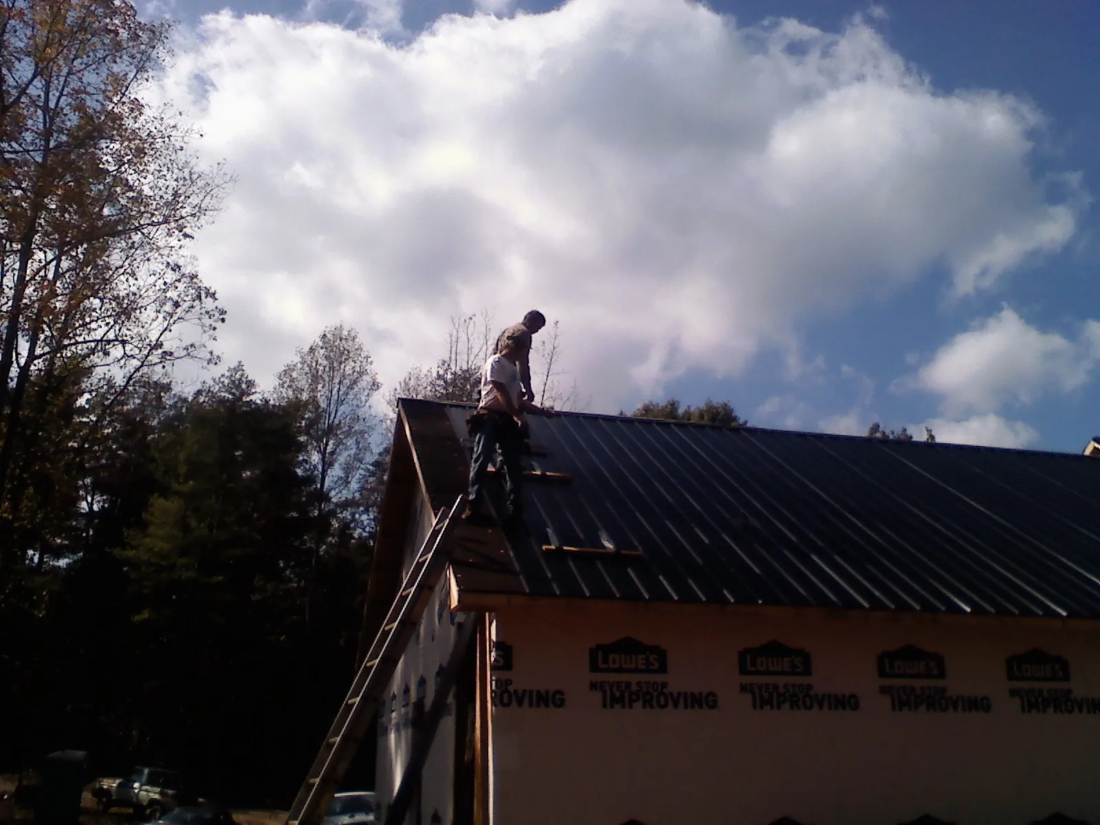 Roofer fastening dark metal panels high against a cloudy sky, from a Roof Inspection job in Surgoinsville