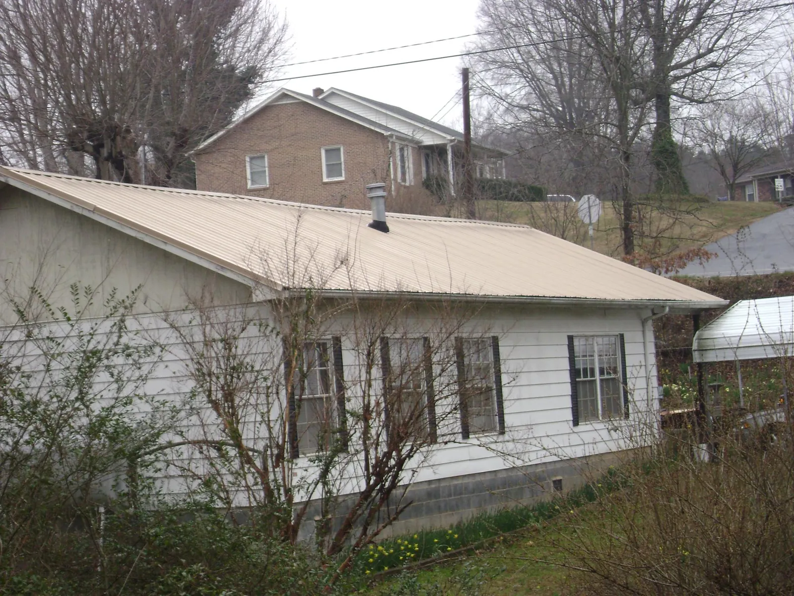 Tan metal roof on a white sided house set into a hillside — Commercial Roofing by Roofing Brothers in Surgoinsville