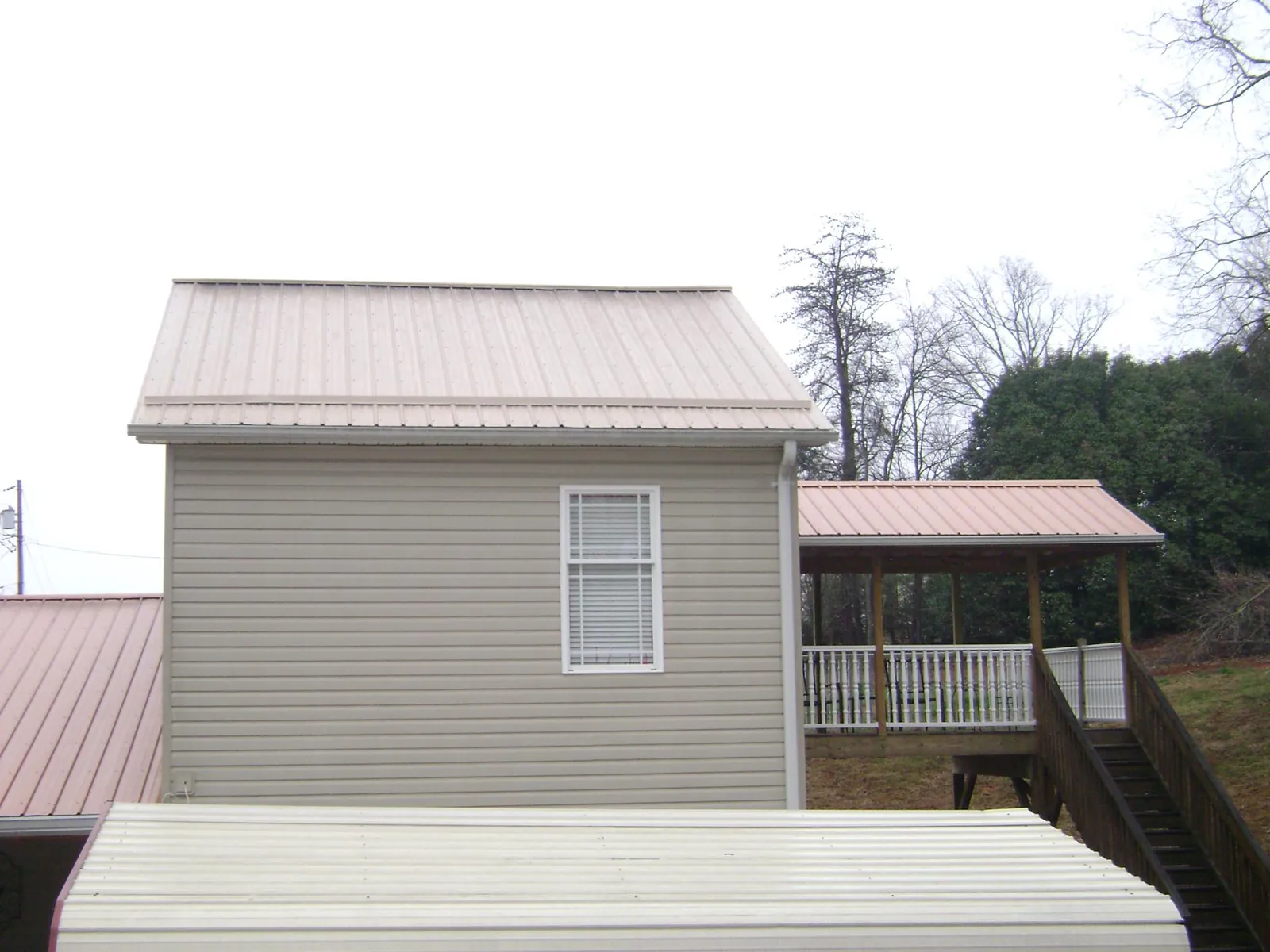 Tan metal roofs on a two story addition and attached porch, from a Roof Replacement job in Surgoinsville